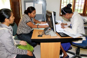 Three women sit at a computer.