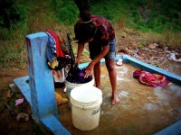 A woman washes clothes under a tap