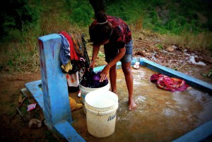 A woman washes clothes under a tap