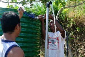 Two men tighten the pipe on a water tank.