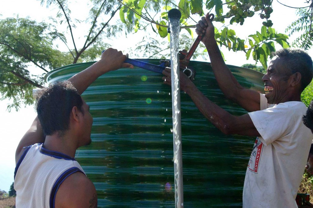 Two men use spanners to adjust the pipes on a large metal water tank