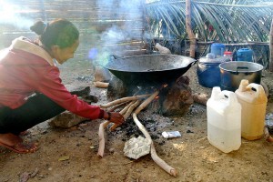 A women cooks in food over the fire, inside a traditional house.