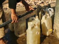Community member uses hose to fill plastic water bottles.