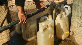 Community member uses hose to fill plastic water bottles.