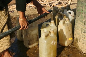 Community member uses hose to fill plastic water bottles.